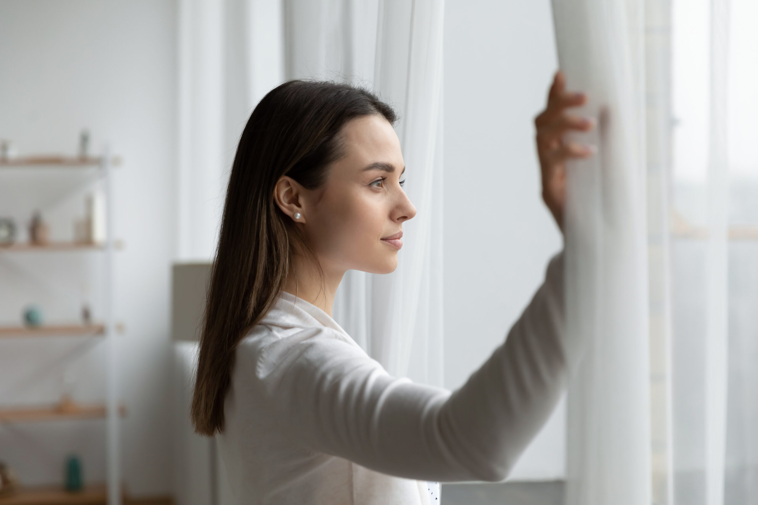 Young woman open curtains look in distance in own home