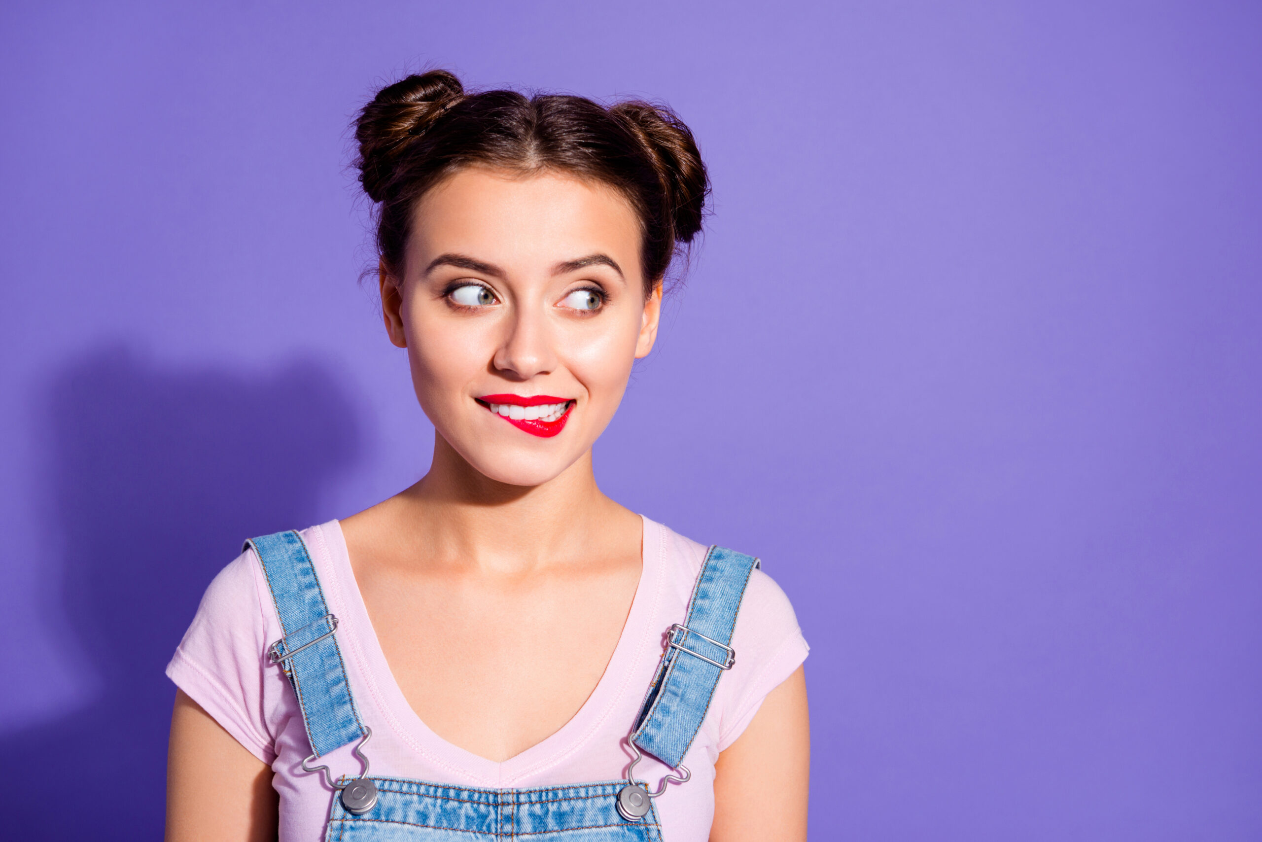 Close up photo beautiful amazing she her lady two buns red pomade bite upper lip tricky mood look side empty space wear casual t shirt jeans denim overalls clothes isolated purple violet background